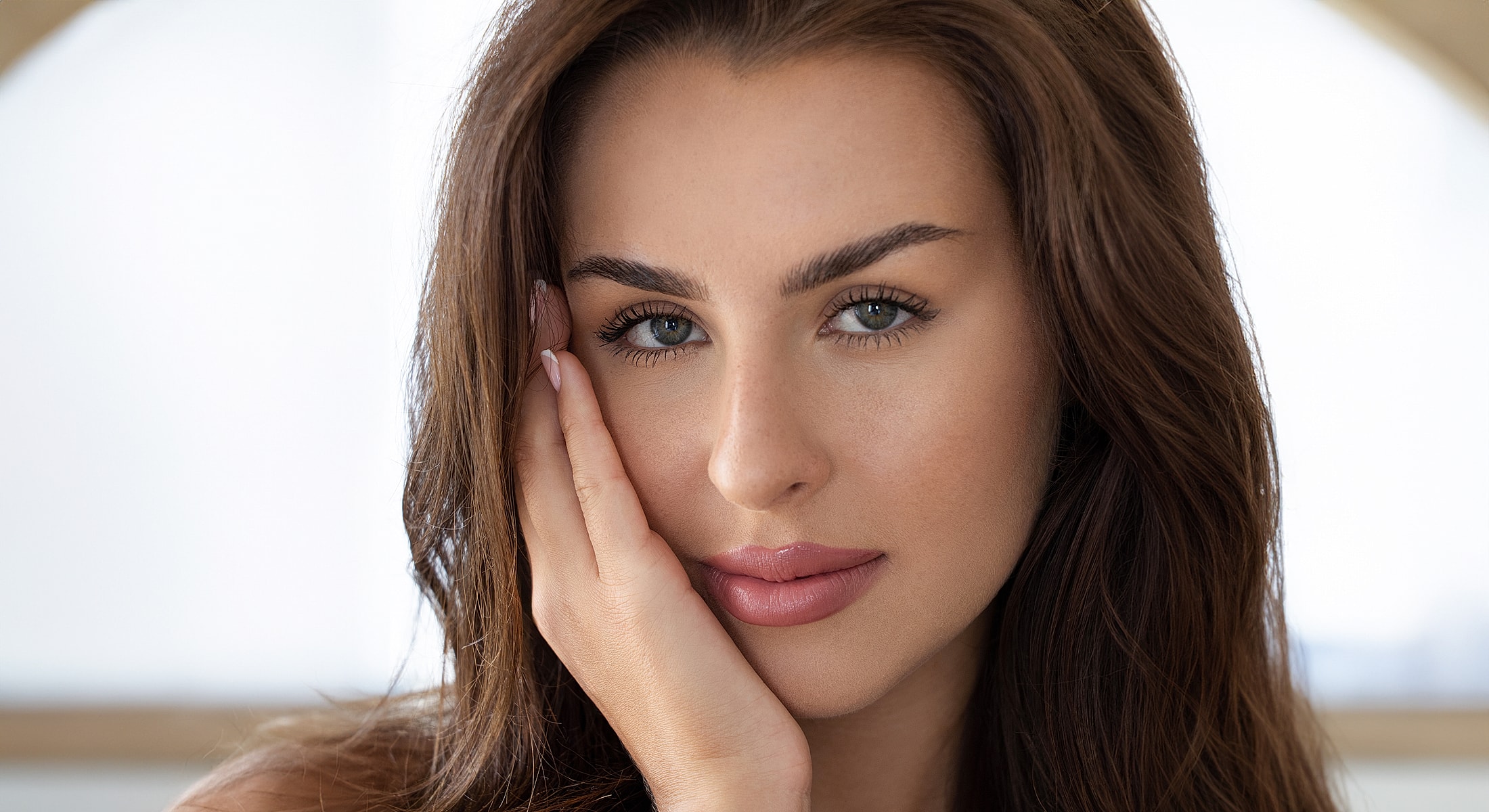 Close-up portrait of a med spa patient model with hand on face.