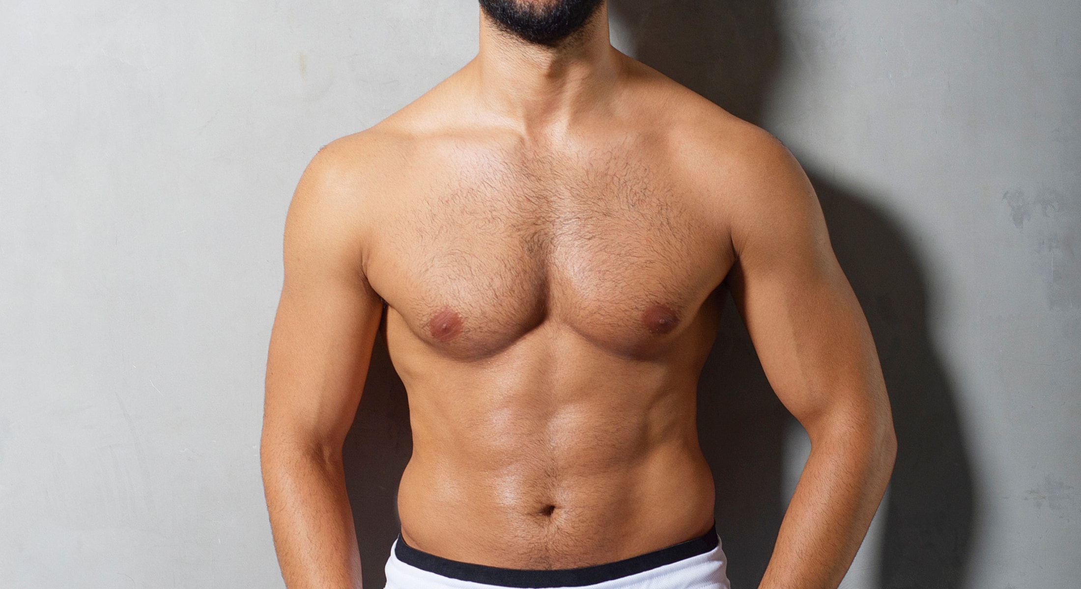 Male gynecomastia surgery patient model showing toned physique against gray background.
