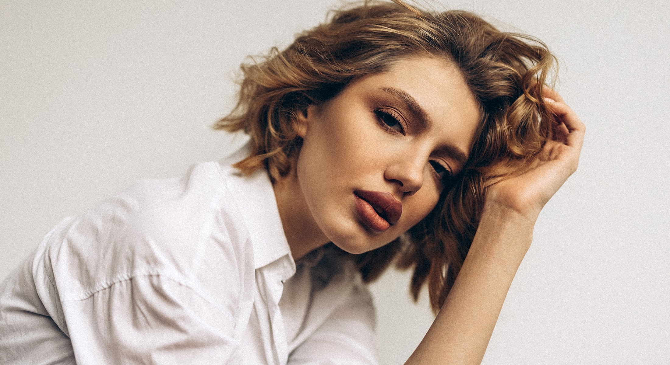 ultrasonic rhinoplasty with wavy hair wearing a white shirt.